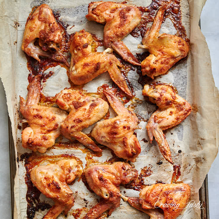 Baked chicken wings, golden brown, on a baking sheet lined with parchment paper.