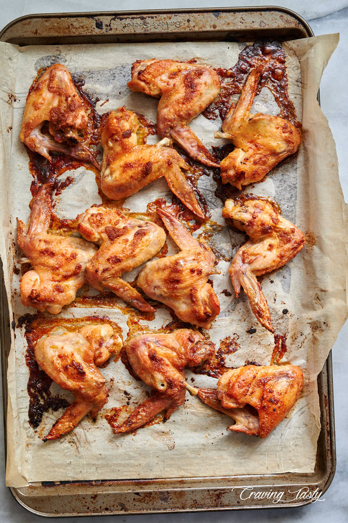 Baked chicken wings, golden brown, on a baking sheet lined with parchment paper.