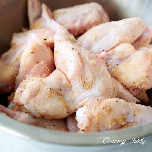 Chicken wings seasoned with salt and spices in a stainless steel bowl.