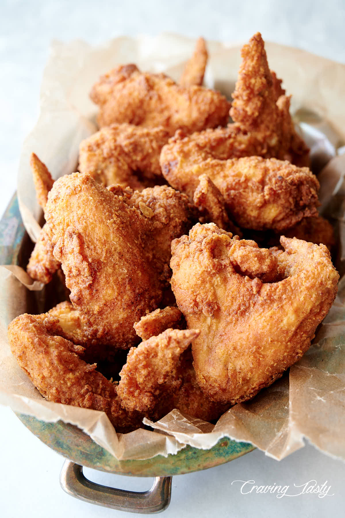 Crispy golden brown whole chicken wings in a basket lined with wax paper.