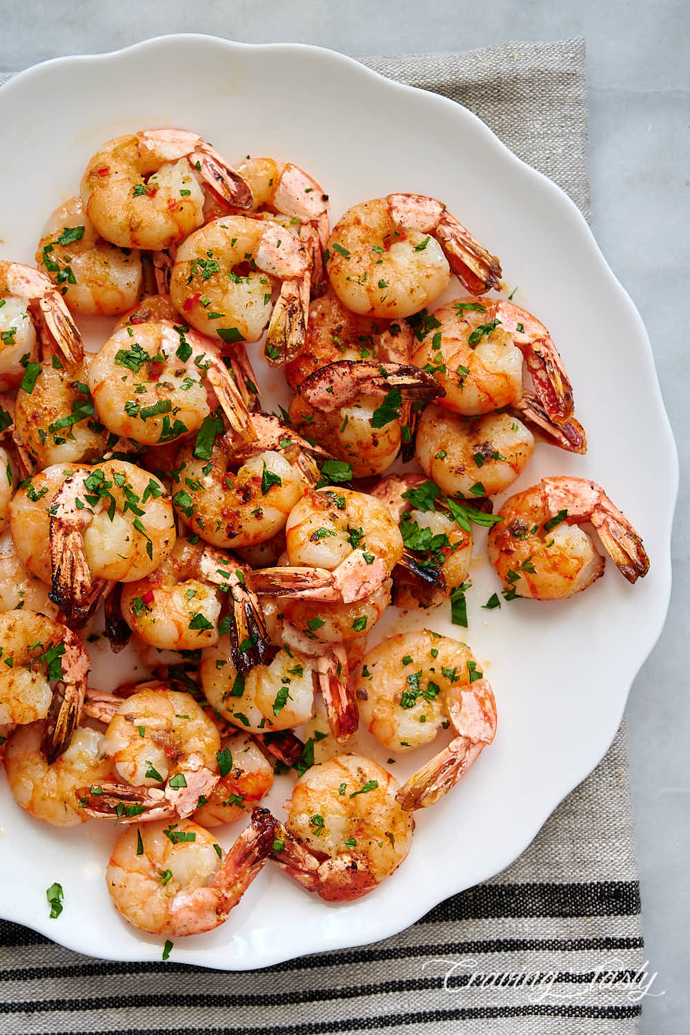 Top down view of a platter with broiled shrimp garnished with chopped parsley.
