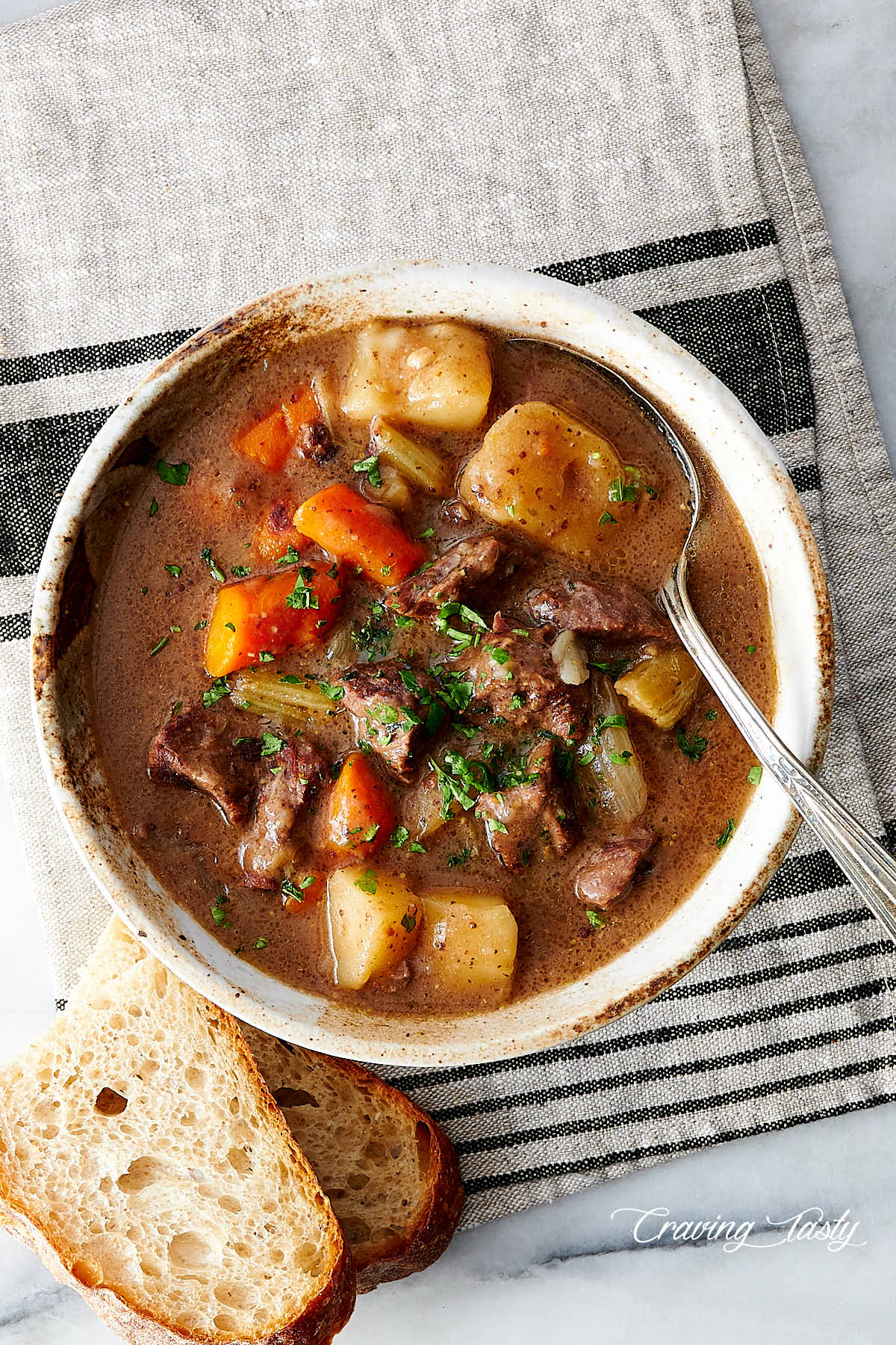 Top down view of a bowl of beef stew, with a spoon and bread on the side.