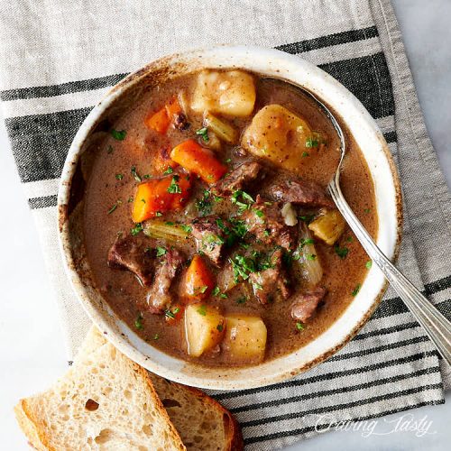 Top down view of a bowl of beef stew, with a spoon and bread on the side.