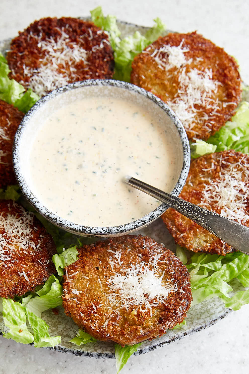 Fried green tomatoes on a plate with greens and bowl of white sauce.