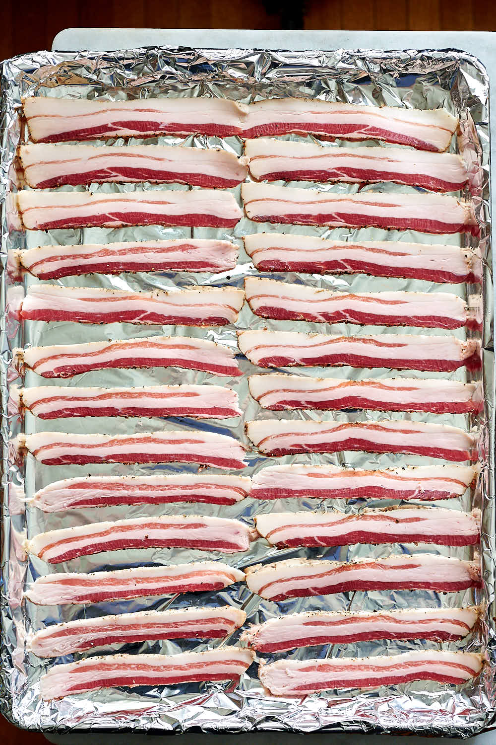 Raw bacon slices on baking sheet