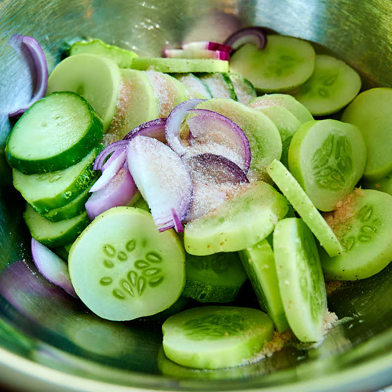 Cucumbers mixed with onions and salt in a bowl.