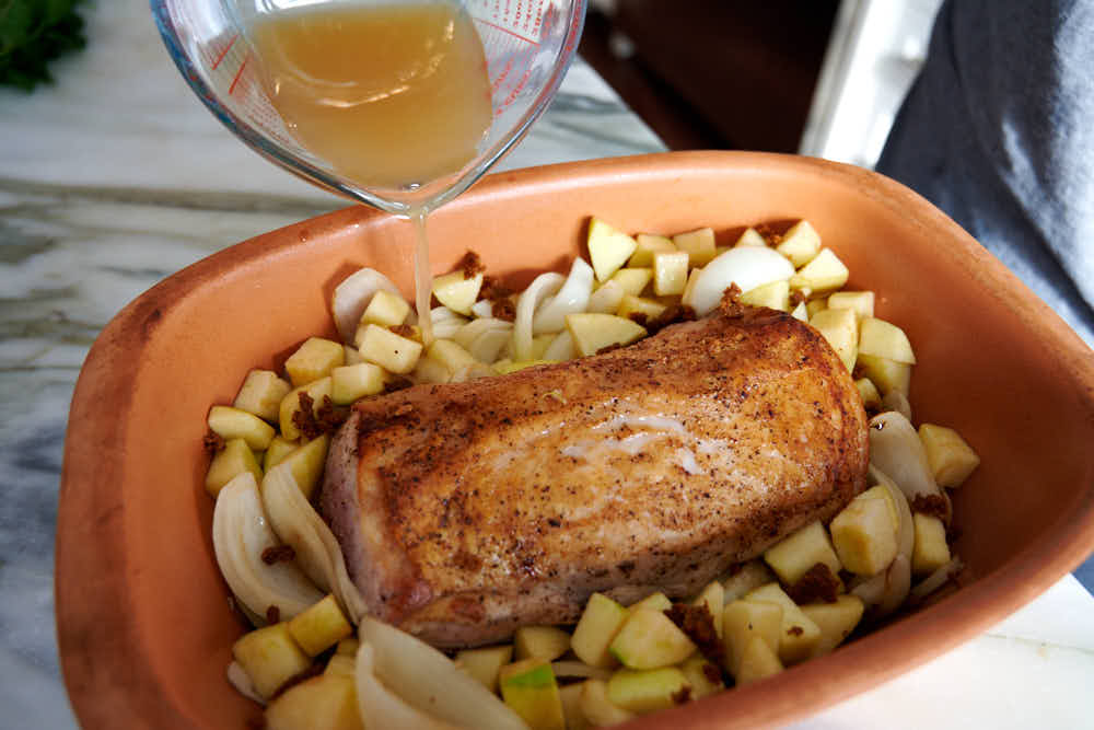 Placing seared pork loin inside braiser on top diced apples and chopped onions.