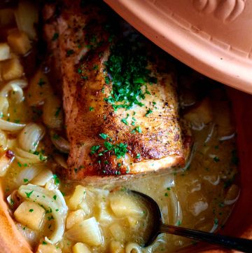 Oven-braised pork loin roast with apples and onions inside a clay baker/Dutch oven