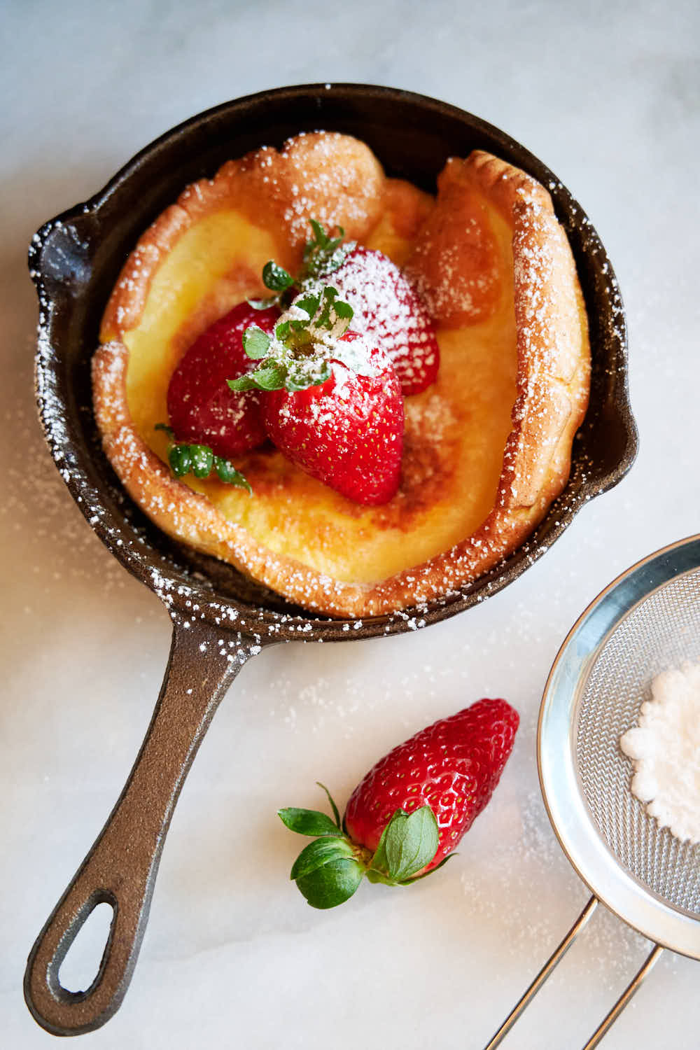 Dutch baby inside a mini cast iron pan topped with strawberries and powdered sugar.