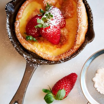 Dutch baby inside a mini cast iron pan topped with strawberries and powdered sugar.