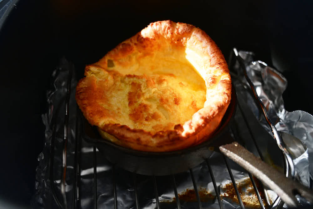 Tall, crispy Dutch baby inside cast iron pan inside an air fryer.