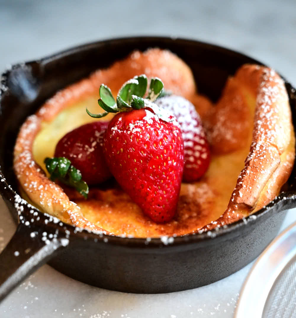 Dutch baby topped with strawberries and powdered sugar inside a cast iron pan.