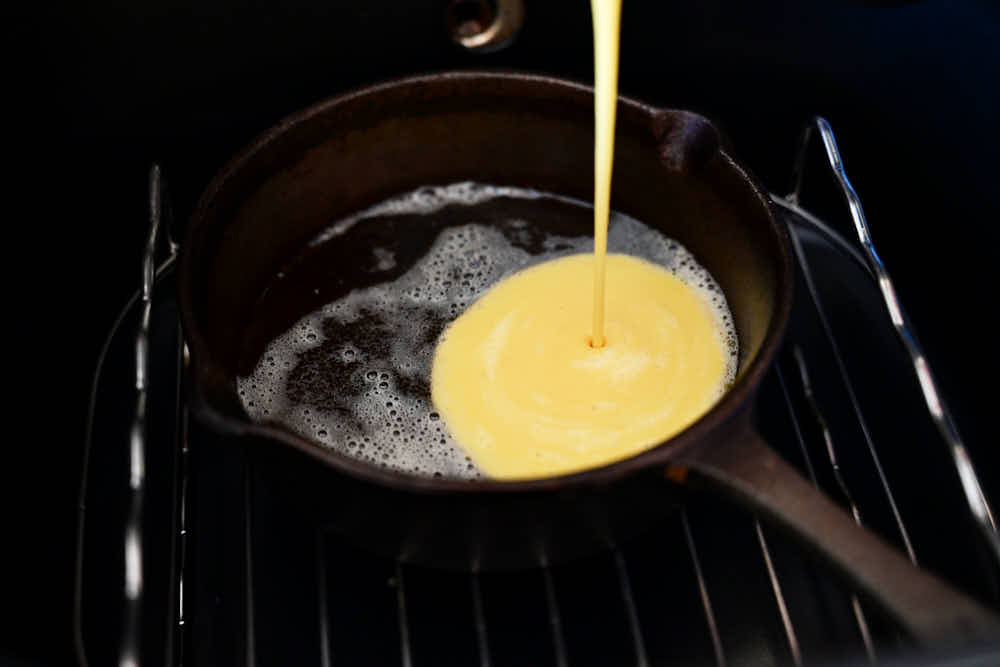 Pouring Dutch baby batter into a hot cast iron pan.