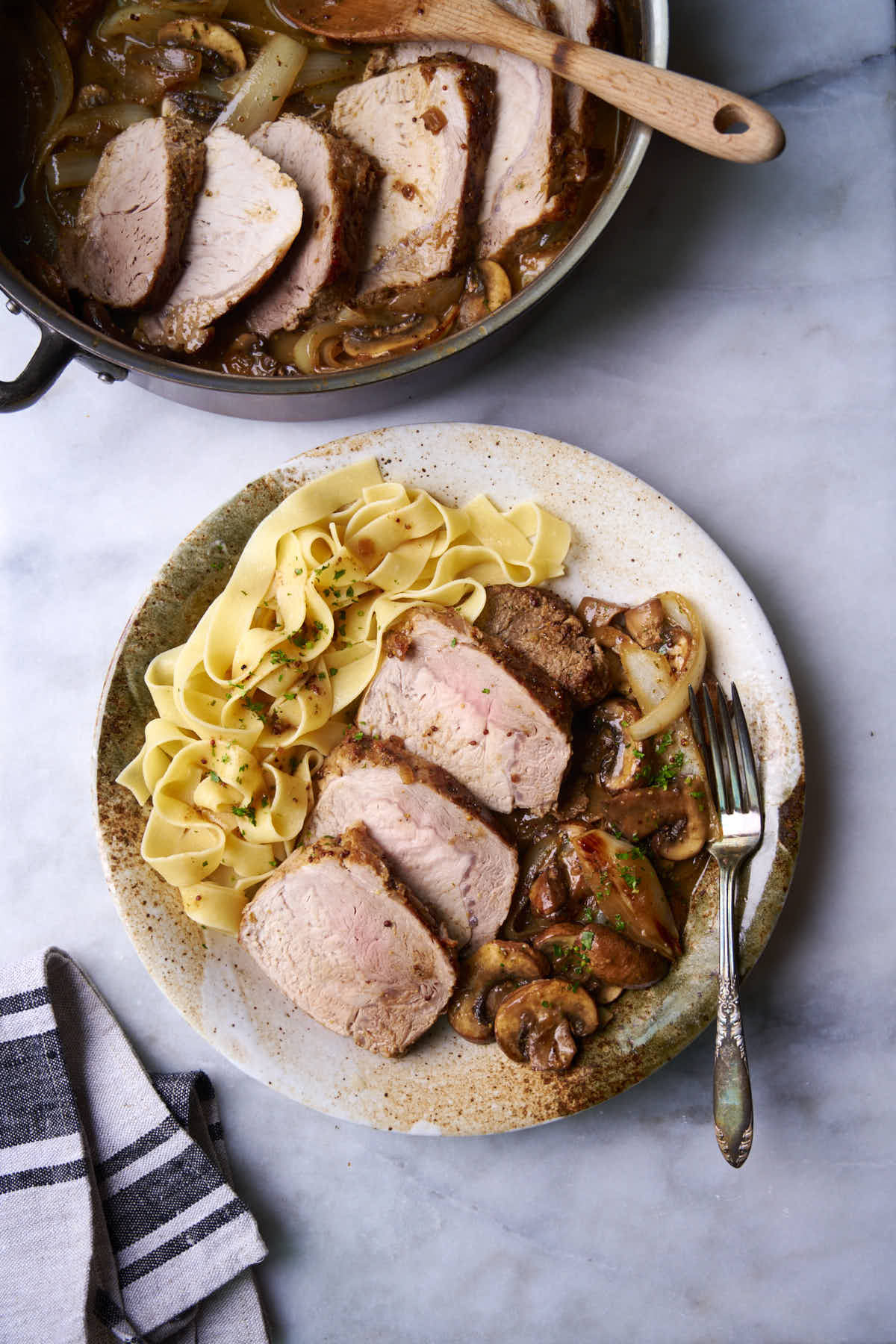 Sliced pork loin roast on a plate served with papardelle pasta and white wine sauce with onions and mushrooms.