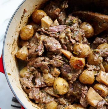 Succulent Beef with Creamy Potatoes in a cast iron pot. The beef is exceptionally tender and succulent. The potatoes are soft and incredibly creamy. All in delicious, buttery, herby sauce.