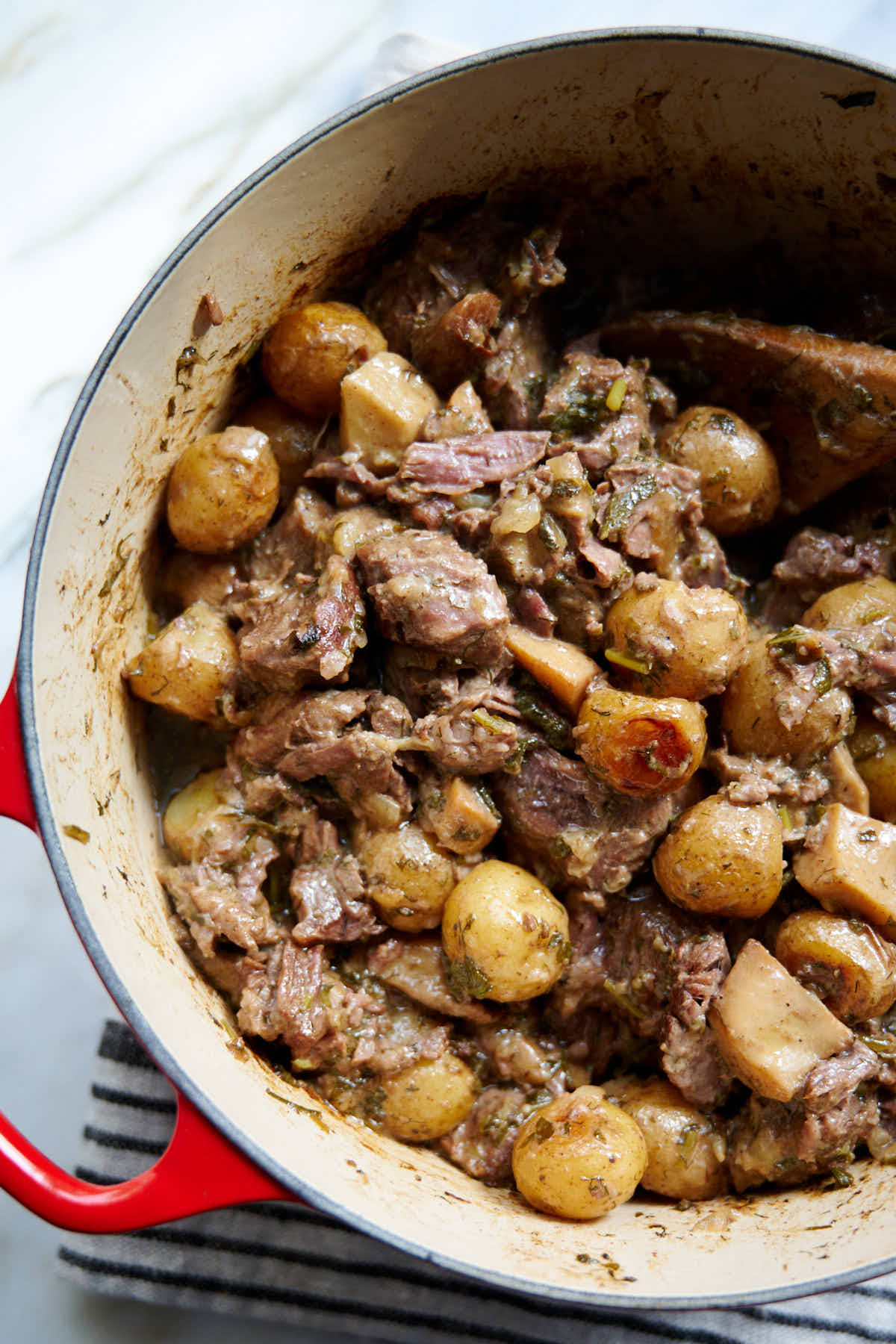 Succulent Beef with Creamy Potatoes in a cast iron pot. The beef is exceptionally tender and succulent. The potatoes are soft and incredibly creamy. All in delicious, buttery, herby sauce.