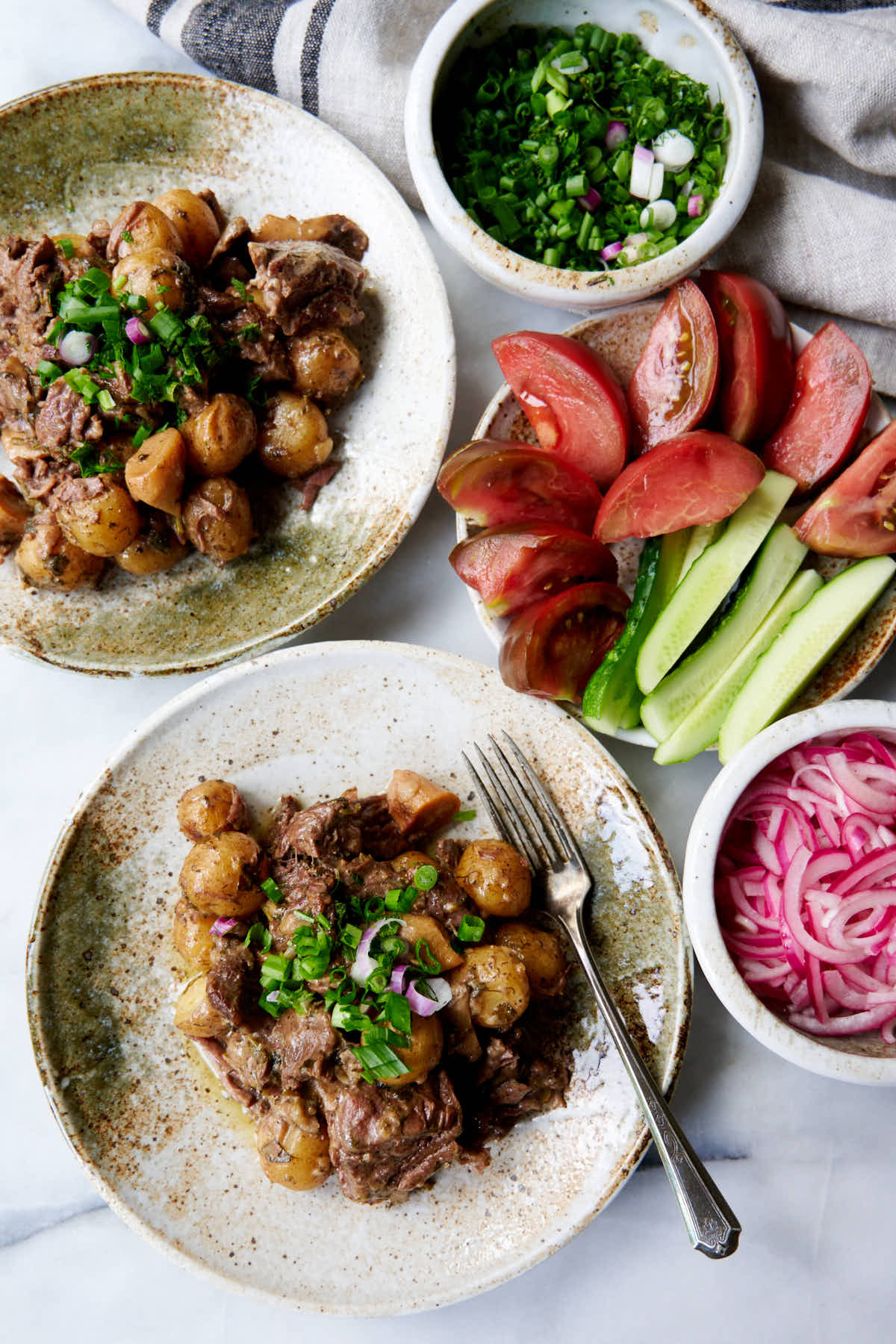 One Pot Beef and Potatoes served on rustic plates with fresh vegetables and pickled red onions.